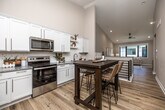 This well-designed two-story home offers four bedrooms and three bathrooms across a generously sized layout. The main floor features an open-concept kitchen and living area, where white shaker-style cabinetry, granite countertops, subway tile backsplash, and stainless steel appliances create a clean, modern kitchen. The adjoining living room is bright and welcoming, with large black-framed windows that invite natural light and outdoor views. Light hardwood flooring flows throughout the main level, lending warmth and continuity to the space. A stylish sliding barn door leads to the dedicated laundry room, which includes a stacked washer and dryer alongside wire shelving for added storage. The upper floor houses the primary bedroom, which is comfortably proportioned and includes a walk-in closet outfitted with wire shelving and carpet flooring. The bathrooms are finished with granite-topped white vanities and glass-enclosed walk-in showers. Additional bedrooms feature plush carpet and neutral tones, offering flexible living arrangements. A utility room with HVAC infrastructure rounds out the lower level. Throughout, the home maintains a consistent palette of soft neutrals, clean trim work, and thoughtful finishes that contribute to a cohesive, move-in-ready atmosphere.