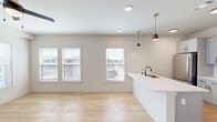 This thoughtfully designed one-bedroom, one-bathroom unit in Hutto, TX offers a clean, modern aesthetic throughout its efficiently utilized single-floor layout. The open-concept living and kitchen area is bathed in natural light from multiple windows dressed with white blinds, complemented by light wood-look flooring and neutral walls that create a bright, airy atmosphere. A ceiling fan adds comfort to the living space, which also features a glass door leading to a private balcony with neighborhood views.

The kitchen is well-appointed with gray shaker-style cabinetry, sleek white quartz countertops, a subway tile backsplash, and a full suite of stainless steel appliances including a refrigerator, dishwasher, range, and built-in microwave. Matte black pendant lights and fixtures add a contemporary touch throughout.

The bedroom features plush carpet flooring, a ceiling fan, and a door with access to an outdoor area, offering a comfortable and private retreat. The full bathroom mirrors the kitchen's design language with gray cabinetry, white countertops, an undermount sink, and matte black hardware, all finished with light tile flooring.

A dedicated in-unit laundry room with a full-size washer and dryer, plus overhead shelving, rounds out this practical and stylish space.