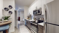 This thoughtfully designed single-floor studio offers a seamless blend of modern style and functional living. The galley-style kitchen is a standout feature, boasting two-tone cabinetry with crisp white upper cabinets and rich dark lower cabinets, complemented by white quartz countertops and a full suite of stainless steel appliances, including a refrigerator, electric range, over-the-range microwave, and dishwasher. Wood-look plank flooring runs throughout the space, lending warmth and visual continuity.

The open living and sleeping area is generously proportioned, with a bold geometric accent wall framing the bedroom space and providing a dramatic focal point. Natural light filters in through a large window dressed with sheer curtains, creating a bright and airy ambiance. Track lighting overhead adds a modern, adjustable element to the room.

The bathroom is clean and contemporary, featuring a floating vanity with wood-toned cabinetry, a white countertop, and sleek matte black hardware that echoes the finishes found throughout the unit.

A spacious walk-in closet with full wire shelving and hanging rods provides excellent storage capacity. A dedicated pantry closet adjacent to the kitchen offers additional storage convenience, rounding out this efficiently designed and stylishly finished space.