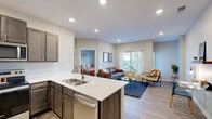 This single-floor residence features a thoughtfully designed open-concept layout that seamlessly connects the kitchen, dining, and living areas. The kitchen is well-equipped with dark wood cabinetry, white quartz countertops, a full suite of stainless steel appliances including a refrigerator, range, microwave, and dishwasher, and a peninsula island with an undermount sink and bar seating. Recessed lighting illuminates the space, which flows directly into the living area finished with light wood-style flooring and neutral-toned walls.

The living area offers generous room for multiple seating arrangements and includes a dedicated workspace nook with a wall-mounted shelf. Large windows allow natural light to fill the space, complemented by sheer curtains for a bright, airy feel.

The bedrooms are carpeted and well-proportioned, each featuring windows with blinds and curtains. One bedroom includes a ceiling fan with a light fixture. The bathroom is finished with tile flooring, a white quartz vanity, dark cabinetry, and a full tub-shower combination with a curtain rod. The overall aesthetic is clean and contemporary throughout.
