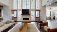The Hillson Farmhouse Apartments clubhouse is a thoughtfully designed community space that blends modern farmhouse aesthetics with refined, welcoming interiors. The grand entrance greets visitors with floor-to-ceiling windows, shiplap walls, and wide-plank hardwood flooring that carries throughout the entire space. A prominent reception desk, clad in rich wood and topped with a decorative penny-tile backdrop, anchors the main lobby alongside a comfortable seating area and direct access to the Mailhouse package room. The great room commands attention with its dramatic double-height windows that flood the interior with natural light and frame views of the outdoor courtyard. A sleek linear fireplace with a rustic wood mantel serves as the focal point, complemented by a mounted television and curated lounge furnishings. Adjacent social areas feature bistro-style seating beneath sculptural pendant lighting, accented by large-scale artwork. The catering kitchen is appointed with quartz countertops, a reclaimed wood ceiling, stainless steel fixtures, pendant globe lights, and open wood shelving. A dedicated game area with foosball and high-top seating offers additional recreational space. Throughout, exposed wood-beam ceilings, barn-style sliding doors, and carefully selected decor reinforce the cohesive farmhouse-inspired character of the clubhouse.