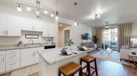 This single-floor residence offers a thoughtfully designed open-concept layout that seamlessly connects the kitchen, dining, and living areas. The kitchen is a standout feature, equipped with crisp white cabinetry, granite countertops, stainless steel appliances, and a central island with bar seating — ideal for casual dining and entertaining. Track and pendant lighting illuminate the space, complementing the warm wood-look flooring that flows throughout the main living areas.

The living room is bright and welcoming, benefiting from a sliding glass door that opens to a private balcony, allowing abundant natural light and outdoor views to enhance the interior ambiance. A ceiling fan adds to the comfort of the space.

The bedrooms are carpeted and cozy, each featuring windows with blinds and sheer curtains that provide both privacy and soft, diffused natural light. The full bathroom is clean and functional, outfitted with a combined tub and shower, a single vanity, and wood-look flooring.

A dedicated in-unit laundry room houses a full-sized washer and dryer side by side, with overhead cabinetry for added storage. Throughout the residence, a neutral color palette and consistent finishes create a cohesive, modern aesthetic that is both practical and comfortable.