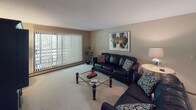 This 2-bedroom, 2-bathroom guest suite is thoughtfully designed to offer comfortable, functional living across a single floor. The living room serves as the heart of the suite, featuring plush carpeting, a large sliding glass door with vertical blinds that allows natural light to fill the space, and room for generous seating arrangements. Adjacent to the living area, the dining space accommodates a full-sized table, complemented by warm neutral walls and framed artwork.

The kitchen is outfitted with classic oak cabinetry providing ample storage, light countertops, a double-basin sink, and black appliances including a full-sized refrigerator and dishwasher. The tile flooring adds durability and easy maintenance to this well-equipped space.

The primary bedroom features a distinctive four-poster iron bed frame, a sliding wood closet, carpeted floors, and warm, subdued lighting that creates a restful ambiance. The second bedroom mirrors this comfort with its own wood-paneled sliding closet and coordinating décor. Both bathrooms are finished with warm wood cabinetry, broad vanity mirrors, light countertops, and tile flooring — one featuring a large mirror and shower-tub combination, the other offering a similarly spacious vanity layout. Together, these spaces create a welcoming and practical guest retreat.