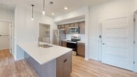This well-appointed single-story home features 3 bedrooms, 2 bathrooms, a dedicated laundry room, and two closets, offering a functional and comfortable layout throughout. The open-concept kitchen and living area serves as the heart of the home, anchored by a large center island with a stainless steel sink, white quartz countertops, and warm wood cabinetry. Pendant lighting accents the island, while recessed lighting illuminates the space. The kitchen is equipped with stainless steel appliances, including a refrigerator, range, and over-the-range microwave, complemented by a classic white subway tile backsplash. The living area flows seamlessly from the kitchen and features wood-look luxury vinyl plank flooring and a sliding glass door that opens to a private balcony with views of the surrounding grounds. The bedrooms are carpeted and filled with natural light from large sliding and standard windows. The primary bedroom is a comfortable size with its own dedicated bathroom. Both bathrooms feature wood-toned vanity cabinetry, white countertops, and wood-look LVP flooring. The in-unit laundry room houses a full-size washer and dryer with overhead shelving for additional storage. Clean white walls and consistent finishes throughout give the home a bright, modern, and cohesive aesthetic.