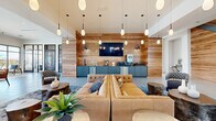 Located at 4590 Trade St in Johnstown, Colorado, this two-story clubhouse delivers a contemporary community gathering space defined by thoughtful design and high-end finishes. The ground floor welcomes visitors through a dedicated entrance that opens into a dramatic main lounge with soaring ceilings, warm natural wood accent walls, and an array of elegant pendant lighting. A built-in wet bar and kitchenette with teal cabinetry and stainless steel appliances anchors one wall, complemented by plush leather seating and organic live-edge coffee tables. A sleek staircase with metal railings connects to the upper level. A standout conference and collaboration area features a stunning live-edge wood communal table bathed in natural light from large windows overlooking an outdoor pool deck. An adjacent lounge captures sweeping exterior views through floor-to-ceiling windows. The upper floor houses an additional living room with a large sectional sofa, curated wall art, and more warm wood paneling, along with a dedicated office space finished with textured wall coverings and carpeted flooring. The game room on the upper level offers a billiards table, a long bar with high seating, wall-mounted TVs, and dramatic pendant fixtures, all set against rich wood feature walls. Light tile flooring flows throughout, tying the entire clubhouse together with a clean, modern aesthetic.