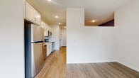 This single-floor unit presents a cohesive, modern aesthetic carried consistently through each room via wood-style luxury vinyl plank flooring and a neutral white and gray color palette. The kitchen is a functional highlight, equipped with a full suite of stainless steel appliances, including a refrigerator, electric range, over-the-range microwave, and dishwasher. White shaker-style cabinetry extends to the upper walls, maximizing storage, while a subway tile backsplash adds a clean, contemporary detail. Recessed lighting illuminates the kitchen and hallway areas effectively.

The living area is open and versatile, offering ample room for various furniture arrangements. A secondary room features a distinctive blue-gray accent wall, adding a touch of character to the otherwise neutral interior. The primary bedroom benefits from natural light through a window and includes closet access, with light-toned wood-style flooring reflecting the space's brightness.

The bathroom is well-appointed with a wood-toned vanity featuring shaker-style cabinet doors, a white countertop, a large mirror, and a full-size soaking tub with a shower combination. Clean white walls and matching flooring maintain the unit's consistent, polished design throughout.