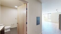 Located at 301 12th Ave in Seattle's Capitol Hill neighborhood, this efficiently designed single-floor unit offers a clean, contemporary aesthetic throughout. Light wood-grain flooring runs across the main living areas, complementing the bright, neutral-toned walls and recessed lighting that together create a fresh and airy atmosphere.

The kitchen is a standout feature, outfitted with sleek dark cabinetry extending from floor to ceiling, stainless steel appliances including an electric range, microwave, and dishwasher, and light countertops that provide a modern contrast. A stacked washer and dryer unit is also incorporated, adding practical convenience.

The living area is open and versatile, bathed in natural light from large windows that offer views of the surrounding Seattle streetscape. The space is clean-lined and ready for personalization.

The bathroom features a floating dark vanity with a white countertop sink, a large mirror with overhead lighting, and durable speckled tile flooring, giving it a polished, functional look. Natural wood-finished doors add warmth throughout the unit.

The entrance area includes a built-in electrical panel and provides a smooth transition into the main living space. Overall, this unit combines modern design with efficient use of space, making it a well-appointed option in the heart of Seattle.