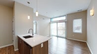 Located at 3420 Broadway Blvd in Kansas City, Missouri, this contemporary single-floor residence offers a thoughtfully designed open-concept layout that seamlessly connects the kitchen, dining, and living areas. Light wood-tone flooring runs throughout, lending a clean and cohesive aesthetic to the entire space.

The kitchen is well-appointed with stainless steel appliances, including a French door refrigerator, electric range, and over-the-range microwave. Warm wood cabinetry provides ample storage, while a peninsula with a white quartz countertop and an undermount sink — accented by stylish pendant lighting — serves as both a workspace and a casual gathering point.

The living area is bright and airy, benefiting from floor-to-ceiling sliding glass doors fitted with vertical blinds that open to an outdoor balcony. Clerestory windows positioned above the sliding doors allow additional natural light to fill the room, while views of the surrounding Kansas City neighborhood enhance the sense of openness.

The bathroom is finished with light tile flooring and a walk-in shower featuring subway tile walls and a frameless glass sliding door, complemented by modern wood-toned cabinetry.

Wall sconces in the dining area add warm accent lighting, completing this modern, move-in-ready space designed for comfortable urban living.