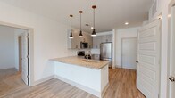 This 2-bedroom, 2-bathroom unit at Sugarloaf Grove in Lawrenceville, Georgia offers a thoughtfully designed single-floor layout with modern finishes throughout. The open-concept kitchen serves as the heart of the home, featuring a large granite-topped island with an undermount sink, sleek gray cabinetry with black hardware, a classic white subway tile backsplash, and a full suite of stainless steel appliances including a refrigerator, range, microwave, and dishwasher. Three stylish pendant lights with brass accents hang above the island, adding a contemporary touch. The kitchen flows seamlessly into the living area, which is brightened by natural light from large windows and finished with light wood-style flooring and a ceiling fan. Both bedrooms are carpeted, generously sized, and include ceiling fans and windows with outdoor views. The primary bathroom offers a granite vanity, walk-in glass shower, and access to a walk-in closet, while the second bathroom features a full soaking tub and shower combination with a matching granite vanity. Clean white walls, light wood-style flooring in the main living areas, and consistent modern hardware tie the entire space together cohesively.