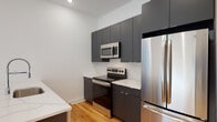 This contemporary 3-floor residence showcases a thoughtfully designed interior with consistent, high-quality finishes throughout. Warm honey-toned hardwood floors flow seamlessly across all levels, complemented by crisp white walls and recessed lighting that create a bright, clean aesthetic.

The kitchen is outfitted with charcoal gray cabinetry extending to the ceiling for ample storage, white quartz countertops, and a full suite of stainless steel appliances including a refrigerator, electric range, and over-the-range microwave. A central staircase with sleek metal railings connects all three floors, serving as a functional architectural focal point visible in the open layout.

Living areas are generously proportioned with tall ceilings and large windows that invite natural light and views of the surrounding urban streetscape. The bathrooms are finished to a high standard — one features a double undermount sink vanity with white quartz countertops, large-format stone tile flooring, and a tub-shower combination with matching tile surround. Additional bathrooms mirror this clean, minimalist design with white cabinetry, modern chrome fixtures, and mirrored medicine cabinets. The bedrooms are spacious and well-lit, offering a calm, neutral canvas throughout this move-in ready multi-floor residence.