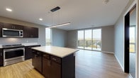 This single-floor residence at 409 N Honey Creek Pkwy in Milwaukee, Wisconsin offers a thoughtfully designed open-concept layout with modern finishes throughout. The living area is a standout feature, with large sliding glass doors that flood the space with natural light and provide direct access to a private balcony overlooking wooded outdoor views — an ideal setting for enjoying Milwaukee's seasonal scenery.

The kitchen is well-appointed with rich dark espresso cabinetry extending to the ceiling, crisp white countertops, a central island with pendant lighting overhead, and a full suite of stainless steel appliances including a refrigerator, range, microwave, and dishwasher. Light wood-look flooring runs throughout the main living areas, complementing the neutral gray tones of the walls.

The bedrooms are carpeted for comfort, each featuring dark-stained solid doors, including a sliding barn-style door in one room. Two bathrooms serve the unit — one with a sleek sliding-glass walk-in shower and dark vanity cabinetry, and a second featuring a full soaking tub. Both bathrooms continue the consistent design language of light flooring and dark cabinetry seen throughout the space.