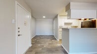 This single-story residence offers a practical and well-organized layout with a neutral color palette throughout. The main living and dining areas are united by durable wood-style plank flooring, creating a cohesive and easy-to-maintain surface underfoot. A sliding glass door opens to a private balcony, allowing natural light to fill the living space and providing a view of the surrounding exterior.

The kitchen is positioned adjacent to the living area and features a peninsula with granite-look countertops that serves as both a workspace and a casual dining option. White cabinetry with brushed hardware lines the walls, complemented by a stainless sink, overhead lighting, and black appliances including a refrigerator. The layout allows for efficient workflow within the space.

The bedrooms are finished with plush carpeting and equipped with ceiling fans fitted with integrated lighting. One bedroom features a window with blinds that admits natural light, while architectural detailing adds visual interest near the ceiling. Both bathrooms are consistent in design, each offering a full-size soaking tub with a tiled shower surround and chrome fixtures, conveying a clean, functional aesthetic throughout.
