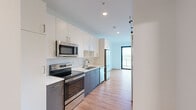 Located at 1237 N Van Buren St in Milwaukee's dynamic East Side neighborhood, this contemporary single-floor unit offers a well-designed open-concept layout that maximizes every square foot. The kitchen and living area flow seamlessly together, anchored by a sleek galley-style kitchen outfitted with stainless steel appliances — including a French door refrigerator, electric range, built-in microwave, and dishwasher. Two-tone cabinetry pairs crisp white upper cabinets with slate-gray lower cabinets, complemented by a white subway tile backsplash and clean countertops. Warm-toned hardwood-style flooring runs throughout the entire unit, lending a cohesive and inviting feel. The living area is bathed in natural light, thanks to floor-to-ceiling sliding glass doors that open directly onto a private balcony, offering elevated views of the surrounding Milwaukee cityscape and neighboring rooftops. A stylish barn door detail adds a modern architectural touch. The full bathroom features a sliding-door shower enclosure with clean, all-white finishes. A wall-mounted mini-split system provides efficient climate control throughout the space. The overall aesthetic is clean, modern, and move-in ready, ideal for those seeking a well-appointed home in the heart of Milwaukee.