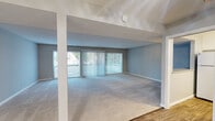 This single-floor residence offers a thoughtfully laid-out interior finished throughout in a calming, neutral gray palette with crisp white trim. The expansive living area is carpeted and bathed in natural light through large sliding glass doors dressed with vertical blinds, which open to an outdoor view. Structural beams add architectural interest to the open feel of this main gathering space. Adjacent to the living area is a transition zone with wood-look flooring leading into the kitchen, which features white cabinetry, stone-look countertops, a built-in microwave, electric range, and a full-size refrigerator — all set atop warm wood-look vinyl flooring. The layout includes multiple carpeted bedrooms, each receiving natural light through windows with vertical blinds. One bedroom includes a double sliding-door closet, while another features a built-in shelving nook. The hallway connects seamlessly to two bathrooms, both outfitted with white vanity cabinetry, stone-look countertops, brushed nickel fixtures, and wood-look flooring. One bathroom features a full tub-shower combination with sliding glass doors. Clean lines, consistent finishes, and an abundance of natural light give the entire space a bright, move-in-ready appeal.