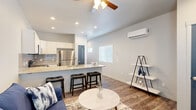 Located at Goodwin Grove in Colorado Springs, CO, this single-floor residence offers a thoughtfully designed open-concept layout that seamlessly connects the living and kitchen areas. The kitchen is a standout feature, showcasing white shaker-style cabinetry, a subway tile backsplash, stainless steel appliances including a refrigerator, microwave, and range, and a generous granite-topped island with an undermount sink and bar seating — ideal for casual dining or entertaining. The living area is finished with durable wood-look flooring, recessed lighting, a ceiling fan, and a wall-mounted mini-split HVAC unit for efficient climate control. Stylish blue accent doors add a distinctive design touch throughout the space. The bedrooms feature plush carpeting and ample natural light from windows with blinds; one bedroom includes a double closet with arched panel doors. The bathroom is outfitted with a full tub-shower combination and brushed nickel fixtures. A dedicated in-unit laundry area with a stacked washer and dryer provides added everyday convenience. Neutral tones and clean finishes create a bright, modern ambiance throughout this well-appointed Colorado Springs residence.