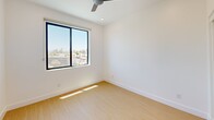 Located in Phoenix, AZ, this modern unit offers four bedrooms and two bathrooms across a single floor. The thoughtfully designed interior features consistent light wood flooring and crisp white walls throughout, creating a clean, cohesive aesthetic.

The kitchen is a standout space, outfitted with stainless steel appliances including a refrigerator, electric range, built-in microwave, and dishwasher. Two-tone cabinetry pairs warm wood upper cabinets with sleek light gray lower cabinets, complemented by white quartz countertops and a sparkling terrazzo-style backsplash with under-cabinet lighting.

The four bedrooms are bright and functional, each featuring recessed lighting and sliding closet doors. Select bedrooms benefit from natural light through large windows, with one room offering outdoor views framed by a ceiling fan. The primary bedroom provides a compact yet efficient layout.

The two bathrooms are clean and modern. One features a glass-enclosed walk-in shower with striking marble-patterned tile surround, while the second includes a full soaking tub with shower combo and chrome fixtures.

A private balcony accessible via sliding glass door offers open views of palm tree-lined streets and a neighboring park, capturing the sunny Phoenix atmosphere. A connecting hallway ties the layout together efficiently.