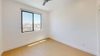 Located in Phoenix, AZ, this modern unit offers four bedrooms and two bathrooms across a single floor. The thoughtfully designed interior features consistent light wood flooring and crisp white walls throughout, creating a clean, cohesive aesthetic.

The kitchen is a standout space, outfitted with stainless steel appliances including a refrigerator, electric range, built-in microwave, and dishwasher. Two-tone cabinetry pairs warm wood upper cabinets with sleek light gray lower cabinets, complemented by white quartz countertops and a sparkling terrazzo-style backsplash with under-cabinet lighting.

The four bedrooms are bright and functional, each featuring recessed lighting and sliding closet doors. Select bedrooms benefit from natural light through large windows, with one room offering outdoor views framed by a ceiling fan. The primary bedroom provides a compact yet efficient layout.

The two bathrooms are clean and modern. One features a glass-enclosed walk-in shower with striking marble-patterned tile surround, while the second includes a full soaking tub with shower combo and chrome fixtures.

A private balcony accessible via sliding glass door offers open views of palm tree-lined streets and a neighboring park, capturing the sunny Phoenix atmosphere. A connecting hallway ties the layout together efficiently.