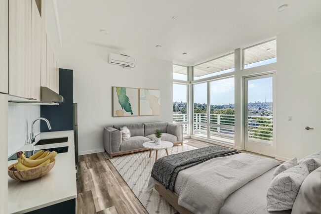 Relax in this inviting bedroom at Anker Ballard, featuring a comfortable bed, cozy couch, and large window that provides natural light and picturesque views. - Anker Ballard