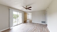This single-floor unit offers a practical and well-organized layout across several thoughtfully designed rooms. The living area is bright and open, finished with light-toned hardwood-style flooring and neutral gray walls that create a clean, versatile aesthetic. A ceiling fan with a light fixture is centrally mounted above a textured ceiling, providing both airflow and ambient lighting. Sliding glass doors lead directly to a balcony overlooking lush tree canopy views, allowing natural light to fill the space generously.

An adjacent area, also with hardwood-style flooring and its own sliding balcony door, offers flexible use as a dining or secondary living space. The kitchen is well-appointed with white cabinetry, light granite-style countertops, and a full suite of stainless steel appliances including a refrigerator, gas range, and dishwasher, all set on matching light wood-style flooring.

The bedrooms feature warm, neutral carpet, ceiling fans, and windows with blinds that bring in natural light. Each bedroom includes closet space, with at least one featuring a full-width reach-in closet with bifold doors. The bathroom is finished with a tiled tub-shower combination, brushed nickel fixtures, and a window for ventilation.