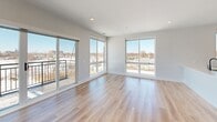 Located in Arlington Heights, IL, this thoughtfully designed 2-bedroom, 2-bathroom residence offers a clean, modern aesthetic throughout. Light hardwood flooring flows seamlessly across the entire space, complementing the bright white walls and recessed lighting overhead.

The open-concept living and dining area is a standout, anchored by oversized floor-to-ceiling windows and a sliding glass door that opens to a private balcony, flooding the space with natural light and offering sweeping views of the surrounding cityscape. The kitchen is well-appointed with a bold two-tone design featuring dark lower cabinetry, natural wood upper cabinets, a white quartz waterfall island with an integrated sink, and a full suite of stainless steel appliances including a gas range and French door refrigerator.

Both bedrooms are generously sized with large windows that continue the theme of abundant natural light and open views. The primary bedroom benefits from direct access to closet space and is served by a sleek en-suite bathroom featuring white tile walls, a glass-enclosed walk-in shower, and wood-toned cabinetry. The second bathroom includes a soaking tub framed by crisp white subway tile. Additional conveniences include a dedicated laundry area, utility room, and multiple closets throughout.
