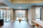 Located at 6101 Richmond Avenue in Houston, TX, this single-floor community space is thoughtfully designed to serve as a social and gathering hub. The open layout seamlessly connects a fully equipped kitchen and dining area, creating a welcoming environment for residents and guests alike.

The kitchen is a standout feature, boasting a striking gold-toned subway tile backsplash, white quartz countertops with an undermount sink, warm wood cabinetry, and a bold dark-topped island with modern bar stools. Pendant lighting and hanging greenery add warmth and personality to the space. A glass entry door leads directly outside, filling the kitchen area with natural light.

The dining area is furnished with a built-in striped banquette, a light-colored rectangular dining table, and mid-century modern chairs. Framed artwork decorates the walls, and a floor-to-ceiling window invites in additional natural light.

A dedicated recreation zone features a full ping-pong table beneath recessed windows with hanging plants, adding a lively, social dimension to the space. Throughout, warm hardwood-style flooring, soft blue ceiling accents, and a neutral gray color palette create a cohesive, contemporary atmosphere. Structural columns and tray ceiling details add architectural depth to this well-appointed community amenity space.