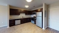 Located at 5105 Gemma Way in Louisville, Kentucky, this single-floor home offers a practical and well-appointed layout designed for comfortable everyday living. The kitchen serves as a functional centerpiece, featuring rich dark-stained cabinetry with ample upper and lower storage, light granite-look countertops, a stainless steel sink, and a full suite of stainless steel appliances including a refrigerator, electric range, built-in microwave, and dishwasher. Light wood-look flooring runs through the kitchen and main living areas, lending a clean and modern aesthetic throughout. The living area is bright and open, benefiting from natural light through blinds-covered windows and a ceiling fan overhead. The bedrooms are carpeted for comfort, each with neutral-toned walls, ceiling fans with light fixtures, and windows that allow natural light to filter in. The bathroom is neatly finished with a dark wood vanity, white countertop, a wall-mounted mirror, brushed nickel fixtures, and a tub-shower combination with safety grab bars. Throughout the home, consistent neutral wall tones, white trim, and coordinated finishes create a cohesive and move-in ready environment.