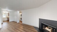 This single-floor unit offers four bedrooms and one bathroom within a efficiently organized layout. The living room serves as the central gathering space, featuring wood-look laminate flooring, a textured ceiling, and a striking black tile-surround wood-burning fireplace as a focal point. A sliding glass door fills the room with natural light and provides direct access to an outdoor area with views of a pool and greenery. An in-unit stacked washer and dryer is conveniently accessible from the living area via a dedicated alcove.

The kitchen is galley-style, equipped with rich wood cabinetry, light stone-finish countertops, a stainless steel refrigerator and range, and a window that allows natural light to brighten the workspace. A pendant light fixture and flush-mount ceiling light provide additional illumination.

The four bedrooms are carpeted and feature textured ceilings and windows for natural light. The primary bedroom includes a closet with a rod system. The shared bathroom is fitted with a full soaking tub and shower combination, white cabinetry for storage, and clean white finishes throughout. A hallway connects the bedrooms and common areas.