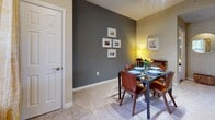 This single-floor residence is thoughtfully laid out across several well-defined living spaces, each with its own distinct character. The dining area makes a strong visual impression with a bold charcoal accent wall, soft carpet underfoot, and track lighting overhead. A glass-top dining table with warm wood chairs anchors the room, complemented by a sideboard and framed artwork that add to the polished atmosphere.

The living room continues the use of deep accent wall coloring, creating a cohesive and modern aesthetic. A ceiling fan provides comfort, while carpeted floors and natural light from nearby windows contribute to a relaxed, inviting ambiance. Built-in shelving on the accent wall adds functional display space.

The kitchen is a galley-style layout featuring rich wood cabinetry, dark granite-look countertops, and hardwood-style flooring. Black appliances, including a refrigerator, range, and over-the-range microwave, are neatly integrated throughout.

The bedroom offers a comfortable, carpeted retreat with natural light from a window framed by dark curtains, providing a calm and restful environment. An entryway wall-mounted coat rack and large mirror offer practical functionality near the unit entrance. The bathroom includes a vanity with a wide mirror and brushed nickel fixtures.
