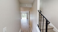 This two-story home offers a well-organized layout across two floors, combining functional design with comfortable living spaces. The main level features a welcoming entryway hallway with light wood-look flooring that flows into a spacious living room bathed in natural light from a large sliding glass door offering views of lush greenery outside. Adjacent to the living room, the kitchen is equipped with dark espresso cabinetry, granite-style countertops, a gas range, and a double sink — offering a practical and stylish cooking space with its own window for natural light. A staircase with a black metal railing connects the main level to the upper floor. Upstairs, two bedrooms are finished with plush carpeting and windows that frame outdoor views. The primary bedroom is generously sized and features dual sliding-door closets, providing ample storage. The second bedroom is cozy and well-lit. Throughout the home, neutral warm-beige tones on the walls create a calm, cohesive ambiance, while textured ceilings add a classic touch. Two hallways on each level ensure smooth circulation throughout the home, making this a practical and inviting two-bedroom residence.