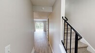 This two-story home offers a well-organized layout across two floors, combining functional design with comfortable living spaces. The main level features a welcoming entryway hallway with light wood-look flooring that flows into a spacious living room bathed in natural light from a large sliding glass door offering views of lush greenery outside. Adjacent to the living room, the kitchen is equipped with dark espresso cabinetry, granite-style countertops, a gas range, and a double sink — offering a practical and stylish cooking space with its own window for natural light. A staircase with a black metal railing connects the main level to the upper floor. Upstairs, two bedrooms are finished with plush carpeting and windows that frame outdoor views. The primary bedroom is generously sized and features dual sliding-door closets, providing ample storage. The second bedroom is cozy and well-lit. Throughout the home, neutral warm-beige tones on the walls create a calm, cohesive ambiance, while textured ceilings add a classic touch. Two hallways on each level ensure smooth circulation throughout the home, making this a practical and inviting two-bedroom residence.