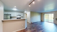Located at 5781 Chapel Valley Rd in Fitchburg, Wisconsin, this well-appointed one-bedroom, one-bathroom unit offers a functional and comfortable single-floor layout. Rich, dark hardwood-style flooring flows throughout the main living areas, lending a warm and cohesive aesthetic to the space.

The combined kitchen and living room area forms the heart of the unit. The kitchen is outfitted with crisp white cabinetry, light quartz-style countertops, a stainless steel refrigerator, electric range, and dishwasher, all centered around a peninsula with a built-in sink — ideal for casual dining and meal prep. The living room is generously proportioned, bathed in natural light from a large sliding glass patio door that opens to an outdoor view, creating a bright and airy atmosphere.

The bedroom is a comfortable retreat, carpeted for warmth, and features a ceiling fan with light fixture, a large window overlooking greenery, and dual closets providing ample storage. Baseboard heating is present throughout the unit.

The bathroom is clean and practical, equipped with a full tub-shower combination featuring stainless grab bars for added accessibility, set above wood-style flooring. Overall, the unit presents a tidy, move-in-ready environment with a straightforward and efficient layout.