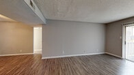 This single-floor, 1-bedroom, 1-bathroom unit offers a practical and comfortable layout across a thoughtfully arranged floor plan. Wood-style plank flooring runs consistently throughout the space, providing a cohesive, low-maintenance foundation in every room.

The unit features two distinct living areas. One is anchored by a sliding glass door that invites natural light and outdoor views, while the other connects directly to the kitchen via an open passageway and is complemented by a ceiling fan. Both areas feature neutral gray walls and textured ceilings.

The kitchen is efficiently designed in a galley-style layout with white cabinetry, dark hardware, dark countertops, a stainless steel sink, and white appliances including a refrigerator, stove, and dishwasher. A secondary door in the kitchen provides additional access to the unit.

The bedroom is generously sized, featuring a ceiling fan, a window for natural light, and multiple doors leading to a dedicated closet and additional storage. The bathroom includes a full tub-shower combo, a vanity with a speckled countertop, and wood-style flooring that matches the rest of the unit.

A hallway connects the main living areas to the private spaces, ensuring a logical and functional flow throughout the home.