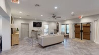 Located at 7642 Zeigler Blvd in Mobile, Alabama, this single-floor space offers a thoughtfully designed layout that balances comfort, function, and style. The great room serves as the centerpiece, featuring large-format porcelain tile flooring in a soft gray tone, recessed lighting, and a ceiling fan. A wall-mounted flat-screen TV anchors the entertainment area, complemented by an elegant gold-framed console table, plush seating, and decorative accents including an ornate carved wall piece. Natural light filters in through multiple windows dressed with white curtains and blinds, creating a bright and welcoming atmosphere.

Adjacent to the great room is a bar area finished with rich dark wood cabinetry, granite countertops, and a row of upholstered bar stools — ideal for hosting and entertaining. The kitchen features matching dark cabinetry, granite counters, tile flooring, and stainless steel appliances, offering a cohesive and functional workspace.

The dedicated exercise room provides a carpeted, well-lit environment equipped with cardio machines including an elliptical and a recumbent bike, along with a wall-mounted TV and windows overlooking the outdoors. This space delivers a comprehensive and versatile environment suited for both relaxation and active living.