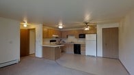 Located at 515-535 W Schindler Pl in Menasha, Wisconsin, this single-floor space offers a practical and functional layout designed for comfortable everyday living. The kitchen is a standout feature, showcasing warm wood-toned cabinetry that extends along the walls and provides ample storage. A peninsula island anchors the center of the kitchen, offering additional counter space and serving as a natural divider between the kitchen and the adjoining living area. The kitchen is equipped with a full suite of appliances, including a white refrigerator, black dishwasher, microwave, and a range with an overhead ventilation hood. The sink is positioned along the back wall beneath the cabinetry, complementing the efficient U-shaped workflow of the space. A ceiling fan with a light fixture is centrally mounted, aiding in air circulation throughout the open area. The flooring transitions from a light-toned surface in the kitchen to carpet in the living area, creating a subtle distinction between the two zones. The neutral wall tones and light-colored countertops contribute to a clean, understated aesthetic. Doorways on either side of the main area provide access to additional rooms, reinforcing the thoughtful and connected flow of the overall floor plan.