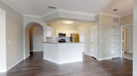 This single-story residence offers two bedrooms and two bathrooms within a thoughtfully designed open floor plan. A welcoming entryway with rich hardwood-style flooring leads into the main living areas, where crown molding and neutral-toned walls create a clean, cohesive aesthetic throughout.

The kitchen features white cabinetry, gray countertops, and a classic subway tile backsplash, complemented by stainless steel appliances including a refrigerator, range, and over-the-range microwave. A peninsula with a raised bar-height overhang connects the kitchen to the living and dining areas, which are defined by an elegant decorative column and an arched pass-through detail.

The living and dining spaces benefit from large windows with blinds that allow generous natural light and views of surrounding greenery. A pendant light fixture anchors the dining area near the front entry door.

Both bedrooms are carpeted for comfort, each offering windows and ample wall space. The two bathrooms are finished with white cabinetry and hardwood-style flooring; one includes a glass-enclosed walk-in shower, while the other features a soaking tub with tiled surround. A dedicated hallway provides a clean transition between the private and shared living areas.