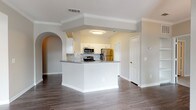 This single-story residence offers two bedrooms and two bathrooms within a thoughtfully designed open floor plan. A welcoming entryway with rich hardwood-style flooring leads into the main living areas, where crown molding and neutral-toned walls create a clean, cohesive aesthetic throughout.

The kitchen features white cabinetry, gray countertops, and a classic subway tile backsplash, complemented by stainless steel appliances including a refrigerator, range, and over-the-range microwave. A peninsula with a raised bar-height overhang connects the kitchen to the living and dining areas, which are defined by an elegant decorative column and an arched pass-through detail.

The living and dining spaces benefit from large windows with blinds that allow generous natural light and views of surrounding greenery. A pendant light fixture anchors the dining area near the front entry door.

Both bedrooms are carpeted for comfort, each offering windows and ample wall space. The two bathrooms are finished with white cabinetry and hardwood-style flooring; one includes a glass-enclosed walk-in shower, while the other features a soaking tub with tiled surround. A dedicated hallway provides a clean transition between the private and shared living areas.