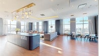 Located on Macleod Trail SE in the heart of Calgary, the Sky Lounge is an expansive, single-floor amenity space offering a refined and versatile environment for socializing and entertaining. The open-concept layout is anchored by warm hardwood flooring throughout and floor-to-ceiling windows that flood the interior with abundant natural light while framing sweeping panoramic views of the Calgary skyline.

The lounge is thoughtfully divided into distinct functional zones. A generous seating area features plush sofas and curved accent chairs arranged around a marble-topped coffee table, complemented by a tray ceiling with warm ambient uplighting. Adjacent to this is a formal dining area with a large dark wood table, seating for eight, and elegant gold oval pendant fixtures overhead. A well-appointed bar and kitchen area includes sleek cabinetry with dark stone countertops and a built-in beverage cooler.

A dedicated games room showcases a full-size billiards table, a dramatic geode-patterned feature wall in deep blue and white, a wall-mounted television, and a high bar with gold-accented stools. Throughout the space, sophisticated designer lighting, navy blue wall paneling, and carefully curated furnishings combine to create a polished, contemporary ambiance that is both functional and visually striking.