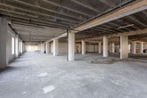 Located at 210–260 W Pershing Rd in Kansas City, Missouri, this single-floor commercial space offers a rare opportunity to experience a large-scale, open-plan environment in shell condition. The layout follows an L-shaped configuration, as revealed by the architectural dollhouse view, providing two substantial wings of contiguous open floor space ideal for flexible buildout planning.

Throughout the interior, rows of structural concrete columns define the floor plate while preserving expansive sight lines across the open concrete slab. The exposed waffle-slab ceiling system is a defining architectural feature, showcasing the building's robust construction and lending an industrial character to the space. Overhead, existing MEP infrastructure—including black iron piping, ductwork, and conduit—is already in place, offering a practical foundation for future tenant improvements.

Perimeter windows along the exterior walls allow natural light to filter into the space, with views overlooking the surrounding Kansas City streetscape. The window-lined sections create bright, open zones well-suited for office, creative, or collaborative uses. Interior partitioned areas with standard doors suggest preliminary demising work has begun in select portions of the floor.

With its raw, adaptable footprint and durable structural bones, this space presents a compelling canvas for a wide range of commercial, creative, or mixed-use buildout concepts.