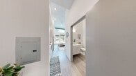 Located at 3803 S Warsaw St in Seattle's Brighton neighborhood, this efficiently designed one-bedroom, one-bathroom unit makes a strong impression through smart use of vertical space and a bright, modern aesthetic. Soaring ceilings throughout amplify the sense of openness well beyond what the floor plan alone might suggest, creating an airy, loft-like atmosphere. Light wood-tone flooring runs continuously through the space, unifying each area with a clean, cohesive look.

The main living area seamlessly integrates sleeping, lounging, and a compact kitchen zone. Full-height windows and a large sliding glass door flood the bedroom with natural light and offer direct views of the surrounding greenery, while clerestory windows positioned high on the walls add an additional layer of brightness. The kitchen features white cabinetry, open shelving, and a full-size refrigerator, maximizing functionality within a compact footprint. A dedicated workspace nook provides a practical area for studying or remote work.

The bathroom is finished with a white floating vanity, wood-look tile flooring, and a shower-tub combination, maintaining the clean, minimalist palette found throughout the unit. The entry corridor houses an electrical panel and offers a transitional space leading naturally into the open main room. Overall, the unit delivers a thoughtfully designed, light-filled living experience well-suited for urban living in Seattle.