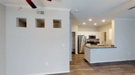 This single-floor residence offers a clean, modern aesthetic with an open-concept design that connects the living and kitchen areas seamlessly. The kitchen is a standout feature, equipped with stainless steel appliances including a refrigerator, range, and over-the-range microwave. White shaker-style cabinetry lines the walls, complemented by dark countertops that add a sophisticated contrast. A central island with a sink provides additional prep space and casual seating potential. Recessed lighting illuminates the kitchen, enhancing its bright and functional atmosphere. A dedicated pantry area offers generous built-in storage, keeping the space organized and efficient. The living area features crown molding along the ceiling, adding a refined architectural touch, along with a ceiling fan for comfort. Decorative square niches are built into the dividing wall, offering display space and visual interest. Rich hardwood-style flooring flows throughout, tying the spaces together with warmth and continuity. The overall ambiance is light, airy, and move-in ready, reflecting a thoughtfully designed layout suited for both everyday living and entertaining.