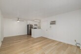 This single-floor unit features a thoughtfully arranged layout across three bedrooms and two bathrooms. Light wood flooring runs consistently throughout the space, lending warmth and visual continuity to every room. The combined kitchen and living area forms the heart of the unit, where a ceiling fan overhead and a sliding glass door opening to a private balcony provide both ventilation and natural light. The living area is bright and open, benefiting from the outdoor view and a wall-mounted air conditioning unit for climate control.

The kitchen is efficiently designed with white cabinetry extending to the ceiling, stainless steel appliances including a refrigerator, range, and dishwasher, and marble-style countertops featuring an undermount sink positioned beneath a window. A peninsula counter separates the kitchen from the living space.

The primary bedroom is generously proportioned and includes a dedicated walk-in closet with built-in shelving and hanging rods. Additional bedrooms are bright and clean, with windows offering outdoor views. Both bathrooms are finished in white, with one featuring a full tub-shower combination. Textured ceilings are present throughout, and hallways connect the rooms efficiently.