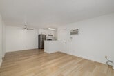 This single-floor unit features a thoughtfully arranged layout across three bedrooms and two bathrooms. Light wood flooring runs consistently throughout the space, lending warmth and visual continuity to every room. The combined kitchen and living area forms the heart of the unit, where a ceiling fan overhead and a sliding glass door opening to a private balcony provide both ventilation and natural light. The living area is bright and open, benefiting from the outdoor view and a wall-mounted air conditioning unit for climate control.

The kitchen is efficiently designed with white cabinetry extending to the ceiling, stainless steel appliances including a refrigerator, range, and dishwasher, and marble-style countertops featuring an undermount sink positioned beneath a window. A peninsula counter separates the kitchen from the living space.

The primary bedroom is generously proportioned and includes a dedicated walk-in closet with built-in shelving and hanging rods. Additional bedrooms are bright and clean, with windows offering outdoor views. Both bathrooms are finished in white, with one featuring a full tub-shower combination. Textured ceilings are present throughout, and hallways connect the rooms efficiently.