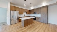 Located in Syracuse, Utah, this well-appointed 2-bedroom, 2-bathroom unit offers a thoughtfully designed single-level layout with modern finishes throughout. The open-concept kitchen and living area serves as the heart of the home, showcasing warm wood-tone cabinetry with matte black hardware, a marble-inspired tile backsplash, white quartz countertops, a center island with pendant lighting, and a full suite of stainless steel appliances. Light hardwood-style flooring runs through the kitchen, living, and secondary bedroom areas, creating a bright and cohesive feel. The spacious primary bedroom features plush carpeting and connects to a well-sized en suite bathroom complete with a walk-in glass-door shower, a wood-tone vanity, and direct access to a generous walk-in closet with built-in shelving. The second bedroom is bathed in natural light from multiple windows and is finished with soft carpeting and a ceiling fan. A second carpeted walk-in closet provides additional storage. The living area opens to a private balcony, offering views of the surrounding community. Recessed lighting, clean white walls, and consistent trim details throughout contribute to the unit's modern, move-in-ready aesthetic.