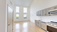 Located at 1300 3rd Avenue North in Nashville, TN, this modern two-story residence offers three bedrooms, two full bathrooms, and a thoughtfully designed open layout spread across two levels. The main floor features a combined kitchen and living area anchored by dramatically high ceilings that amplify the sense of openness. The kitchen is outfitted with gray shaker-style cabinetry, a white quartz countertop, stainless steel appliances including a range, microwave, and French door refrigerator, and a classic subway tile backsplash. Light oak hardwood flooring runs continuously throughout both floors, lending warmth and cohesion to the space. The living area benefits from floor-to-ceiling windows that flood the room with natural light and offer views of the surrounding neighborhood. Bedrooms are bright and airy, each featuring large windows with outdoor views, with the primary bedroom offering generous double closets. Both full bathrooms are finished consistently with gray vanities, white countertops, and tub-shower combinations. The upper level, accessed via staircase, provides additional bedroom space with vaulted ceilings. The overall aesthetic is clean, contemporary, and minimal, with a neutral white palette throughout.