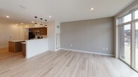 Located at 1–65 Tracy St in Rochester's vibrant East End neighborhood, this modern single-floor unit offers a thoughtfully designed open-concept layout finished with contemporary details throughout. Light-toned hardwood flooring flows seamlessly across the main living areas, creating a bright and cohesive aesthetic.

The kitchen is a standout feature, outfitted with rich dark-toned shaker-style cabinetry, light quartz countertops, and a full suite of stainless steel appliances including a refrigerator, electric range, and over-the-range microwave. A breakfast bar peninsula provides additional counter space and serves as a natural divider between the kitchen and the open living area. Pendant lighting above the peninsula adds a stylish, functional touch.

The living area is generously proportioned, bathed in natural light from large windows that frame views of the surrounding Rochester cityscape. The space is finished with neutral gray accent walls and recessed lighting, contributing to a clean, modern ambiance.

The bathroom features tile flooring, a walk-in shower with a grab bar, and crisp white walls, combining practicality with a clean, minimalist design. Throughout the unit, the interplay of natural light, contemporary finishes, and an efficient open floor plan creates a comfortable and functional living environment well-suited to urban living.