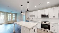 This well-appointed 2-bedroom, 2-bathroom residence in Jacksonville, FL offers a thoughtfully designed single-floor layout with modern finishes throughout. The open-concept kitchen serves as the centerpiece, showcasing crisp white shaker cabinetry with matte black hardware, a large quartz-topped island with pendant lighting, subway tile backsplash, and a full suite of stainless steel appliances including a range, built-in microwave, and refrigerator. Light wood-tone flooring flows through the kitchen and living areas, complementing the neutral color palette. The living room benefits from natural light through windows with exterior views and is equipped with a ceiling fan. The generously sized primary bedroom features its own ceiling fan, multiple windows, and direct access to a well-appointed en-suite bathroom with a double vanity, dark cabinetry, white quartz countertops, a glass-enclosed walk-in shower with subway tile, and wood-look flooring. A spacious walk-in closet with wire shelving and carpet flooring accompanies the primary suite. The second bedroom is carpeted with a ceiling fan and a bright window. The second bathroom mirrors the refined design with a single vanity, subway tile shower, and wood-look flooring.