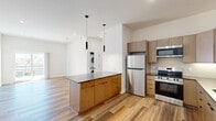 Located at 220 N Walton Blvd in Bentonville, Arkansas, this thoughtfully designed 2-bedroom, 1-bathroom residence offers a clean, modern aesthetic across a well-utilized single floor. Warm, multi-tone wood-look flooring flows seamlessly throughout every room, complementing the crisp white walls and contemporary finishes.

The open-concept kitchen and living area serves as the heart of the home. The kitchen is outfitted with flat-front cabinetry in a natural tan finish, dark quartz countertops, a classic subway tile backsplash with under-cabinet lighting, stainless steel appliances including a refrigerator, range, microwave, and dishwasher, and a matte black faucet. A central island with additional cabinetry provides extra prep space and storage. An in-unit stacked washer and dryer is conveniently tucked nearby. The open living area features recessed lighting and a clean, versatile layout.

Both bedrooms are well-proportioned, each with ceiling fans, generous closet storage — including a full built-in wardrobe — and windows that invite natural light. The primary bedroom offers a comfortable, spacious feel.

The bathroom is finished with a dual-sink vanity featuring dark stone countertops, warm wood cabinetry, matte black fixtures, and a frameless mirror, all reflecting the home's cohesive modern design language.