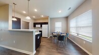 This single-floor residence offers a thoughtfully designed open-concept layout that seamlessly connects the kitchen, dining, and living areas. The kitchen is well-equipped with dark espresso cabinetry, white appliances including a refrigerator, range, built-in microwave, and dishwasher, along with light countertops and a peninsula that provides additional prep space and a natural divider between the kitchen and dining area. A pendant light above the peninsula adds a decorative touch, while recessed lighting illuminates the space throughout. The adjacent dining area benefits from natural light streaming through multiple windows with blinds, creating a bright and welcoming atmosphere. The living room features durable wood-style flooring, neutral walls, and a ceiling fan, providing a comfortable and functional gathering space. Both bedrooms are carpeted and include ceiling fans and windows for natural light, offering a calm and restful environment. The bathroom is finished with tile flooring, a dark vanity cabinet, a large mirror, and a well-lit vanity fixture. A generously sized walk-in closet with wire shelving provides ample storage. Wood-style flooring flows throughout the common areas, tying the space together with a cohesive, contemporary aesthetic.