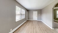 Located at 6000 Tabor Ave, Unit 4 in Philadelphia's 19111 neighborhood, this one-bedroom, one-bathroom unit offers a practical and well-organized layout across a single floor. The living room is a welcoming entry point, featuring light wood-tone laminate flooring, neutral gray walls, and large windows fitted with blinds that invite generous natural light and views of the surrounding greenery. Baseboard heating runs throughout, and the space flows naturally toward a compact kitchen equipped with warm wood cabinetry, a white refrigerator, a gas range, and a sink — all visible in the dollhouse view. An arched doorway adds a subtle architectural detail connecting the living area to the hallway. The bedroom is carpeted for comfort, painted in the same soft gray palette, and includes a ceiling fan with light fixture along with a wide double window that further enhances natural light. The full bathroom is finished with classic white tile on both the floor and walls, a wood-vanity with sink, toilet, and a bathtub/shower combination, plus a window for ventilation. The hallway connects all rooms efficiently, completing a compact yet functional floor plan well-suited for everyday living.