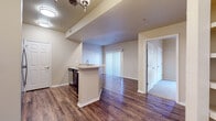 This single-story unit is designed with an open, functional layout that connects the kitchen and living areas seamlessly. The kitchen serves as a central hub, featuring a peninsula with a built-in sink, stainless steel appliances including a refrigerator, range, and microwave, dark espresso cabinetry with tile backsplash, and durable wood-look flooring that extends throughout the main living spaces. A chandelier-style light fixture and recessed lighting provide ample illumination in this area.

The open living space flows naturally from the kitchen toward a windowed wall fitted with vertical blinds, allowing natural light to fill the interior. Built-in shelving adds a practical architectural detail near the transition between rooms.

The bedrooms are finished with plush carpeting and each includes a ceiling fan, windows with horizontal blinds for natural light and privacy, and closet access. The rooms offer a comfortable, well-proportioned sense of space.

Two bathrooms are present in the unit, each sharing a consistent design aesthetic with dark espresso vanity cabinetry, light countertops, large mirrors, brushed nickel fixtures, and wood-look flooring. The overall ambiance of the unit is clean, neutral, and move-in ready.